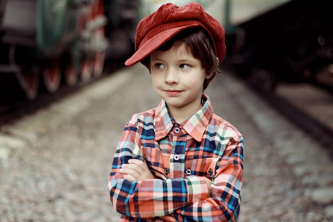 A boy is standing and wearing a red cap