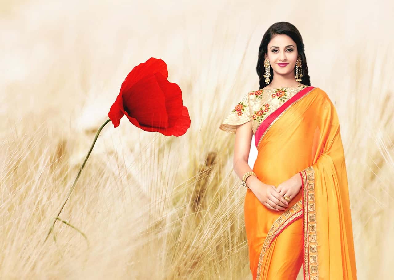 A beautiful woman wearing a yellow saree is standing and smiling